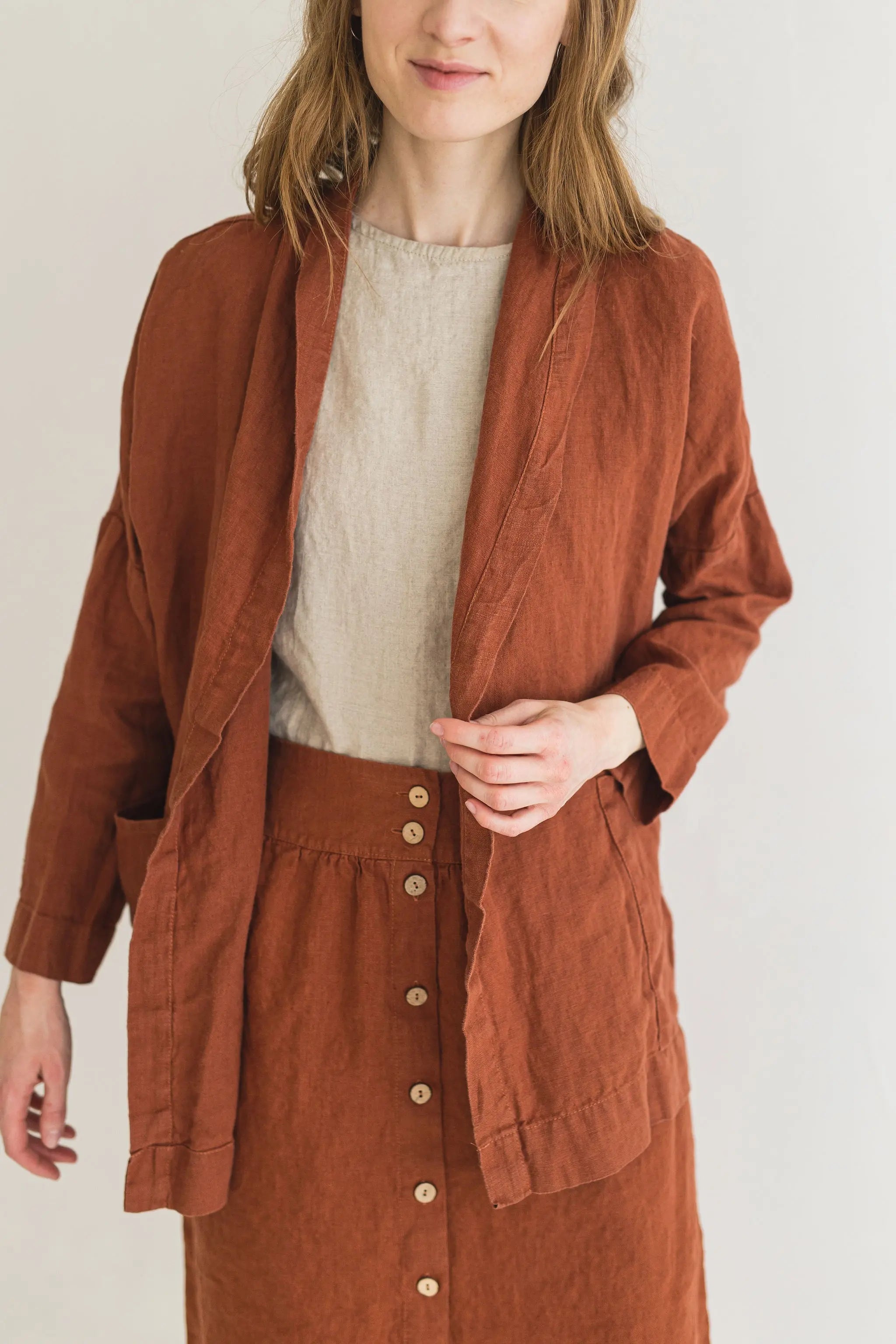 Woman wearing a brown jacket over a beige sweater on a white background