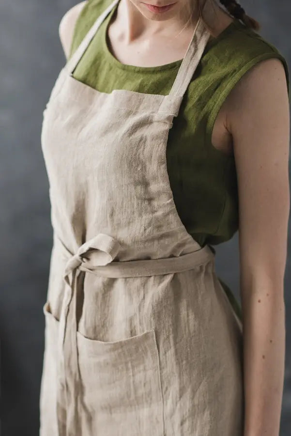 A close up of a woman wearing a Bib style long linen apron with a front pocket and adjustable straps.