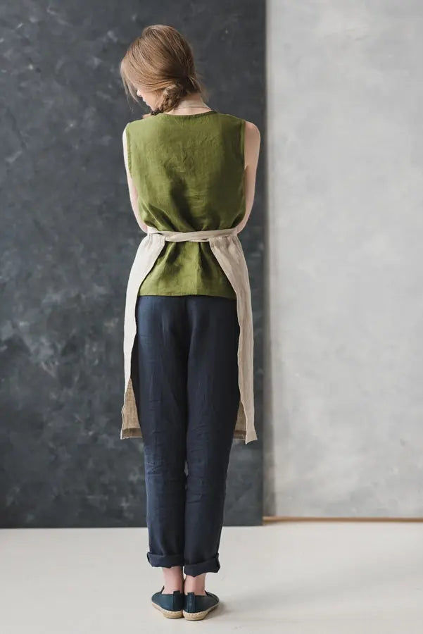 A woman facing away while wearing a Bib style long linen apron with adjustable straps.