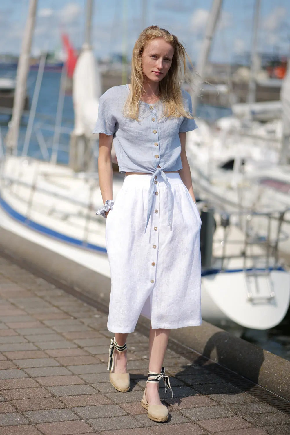 Model walking near yachts in breathable linen outfit.