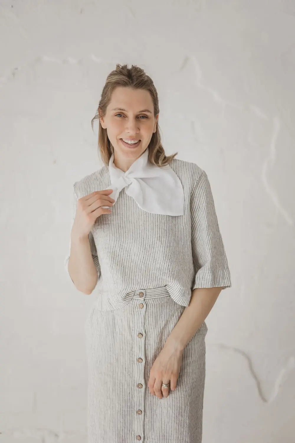 Woman wearing light white linen neckerchief with sewn loop styled over striped linen top and skirt