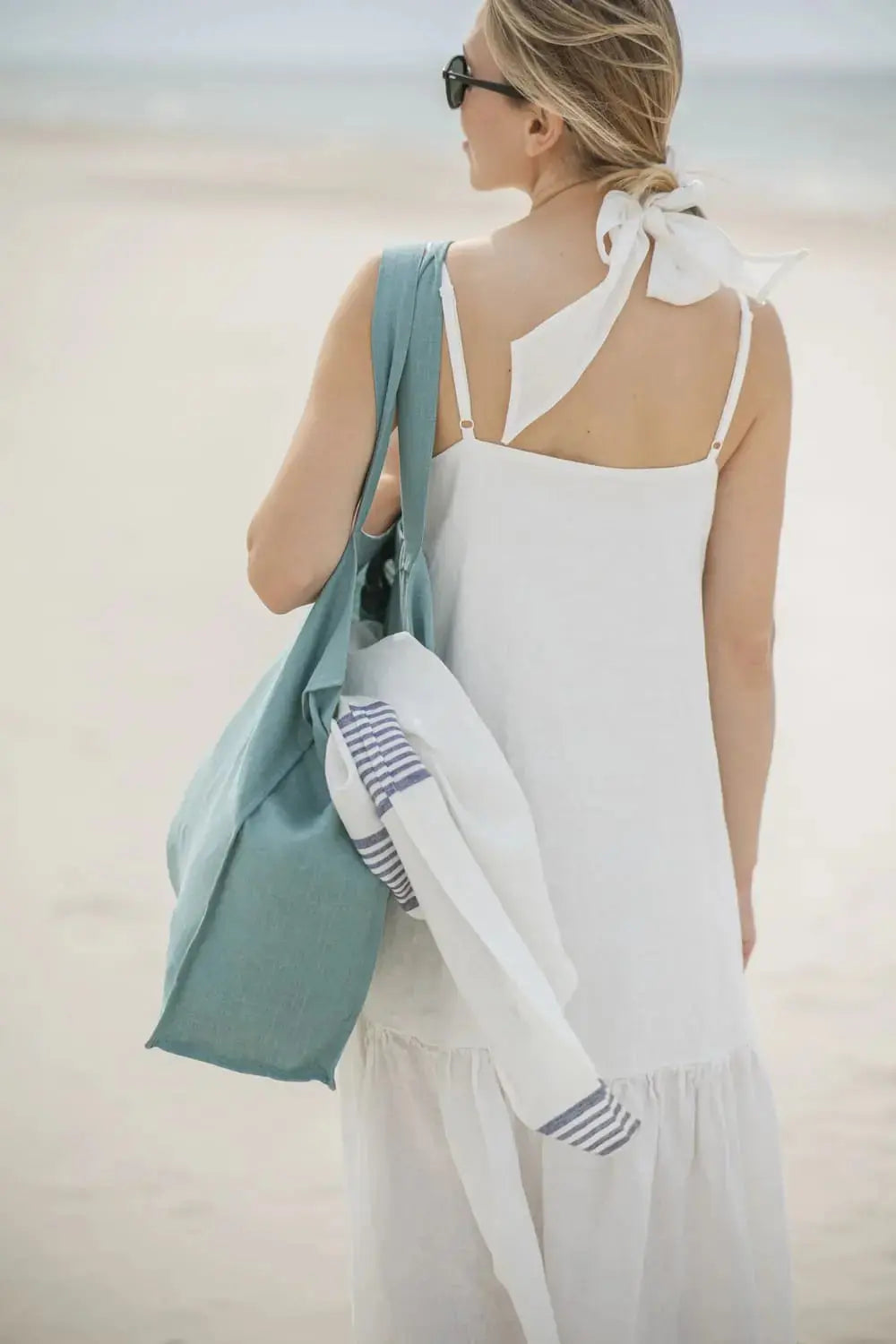 Woman on the beach carrying a blue striped linen towel in a tote bag
