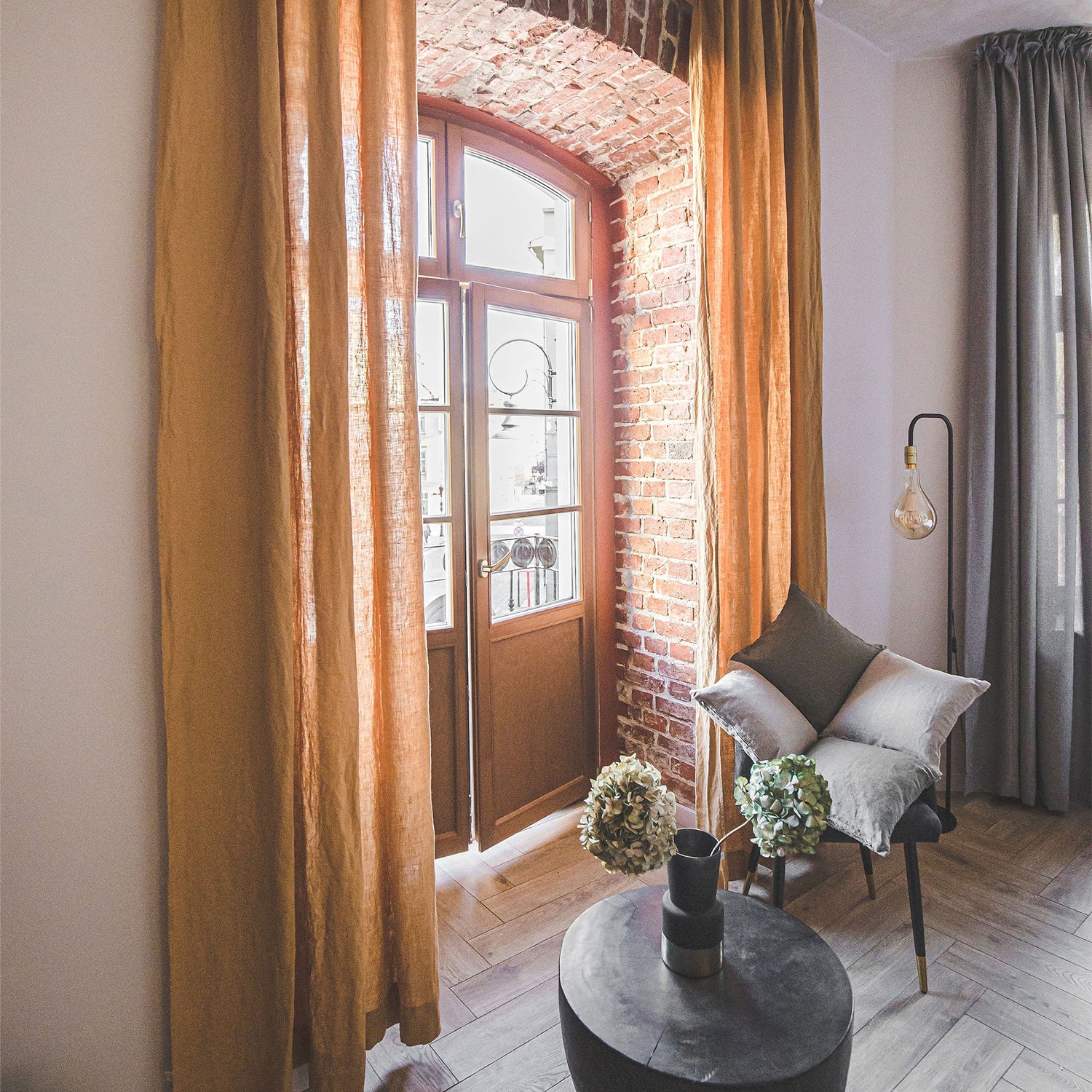 Medium weight linen curtains in a cozy mustard color hanging on a balcony door behind a chair and a coffee table