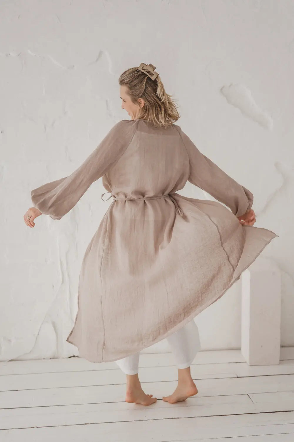 Full back view of a natural linen kaftan in motion, flowing silhouette with waist tie