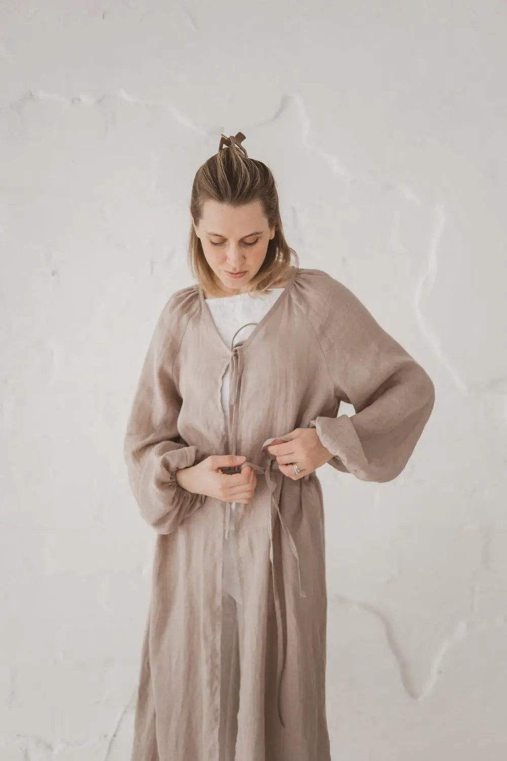 Woman tying the waist tie on a natural linen kaftan, upper body front view