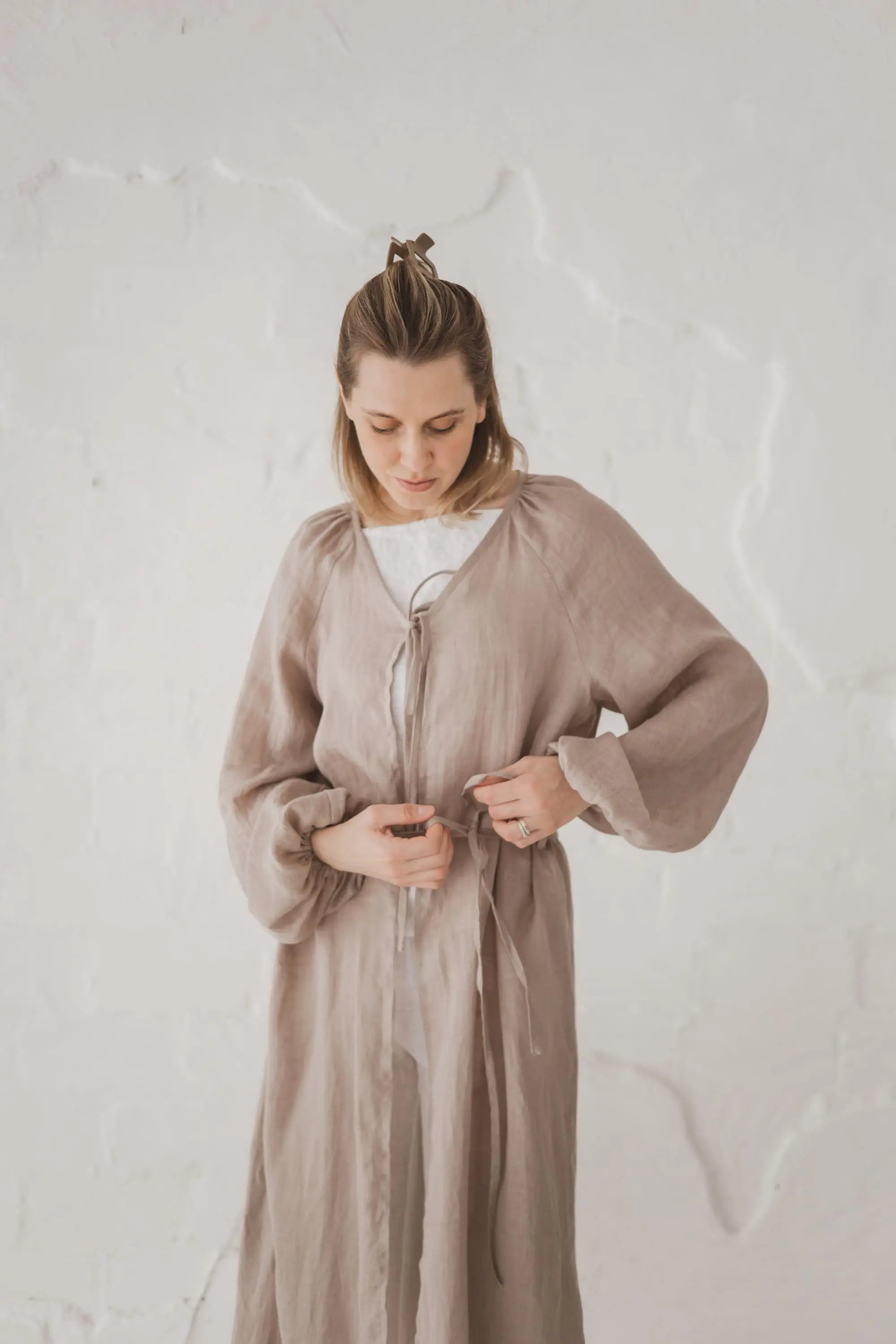 Woman tying the waist tie on a natural linen kaftan, upper body front view