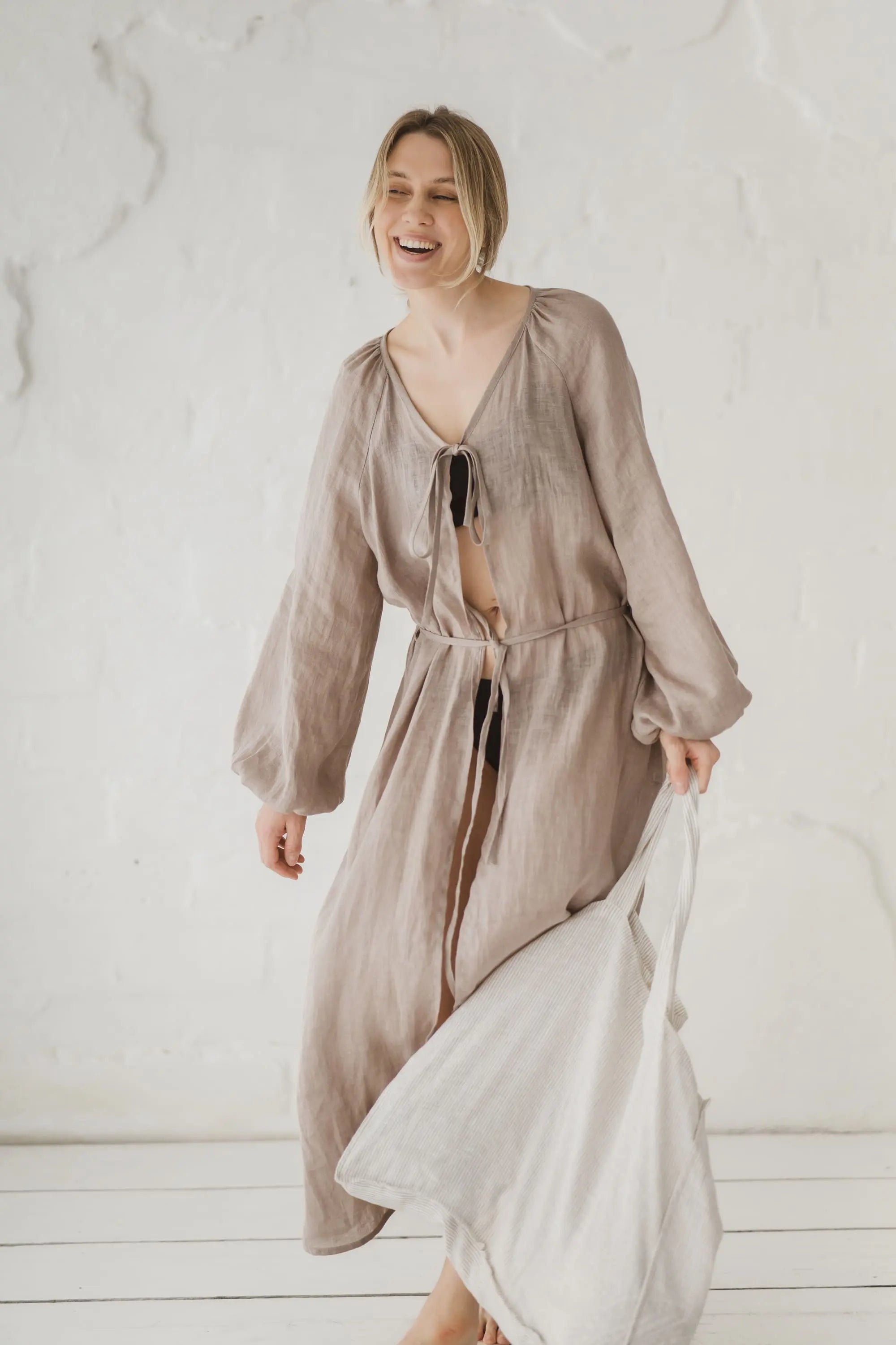 Woman in a natural linen kaftan with waist tie, laughing, full length front view in motion