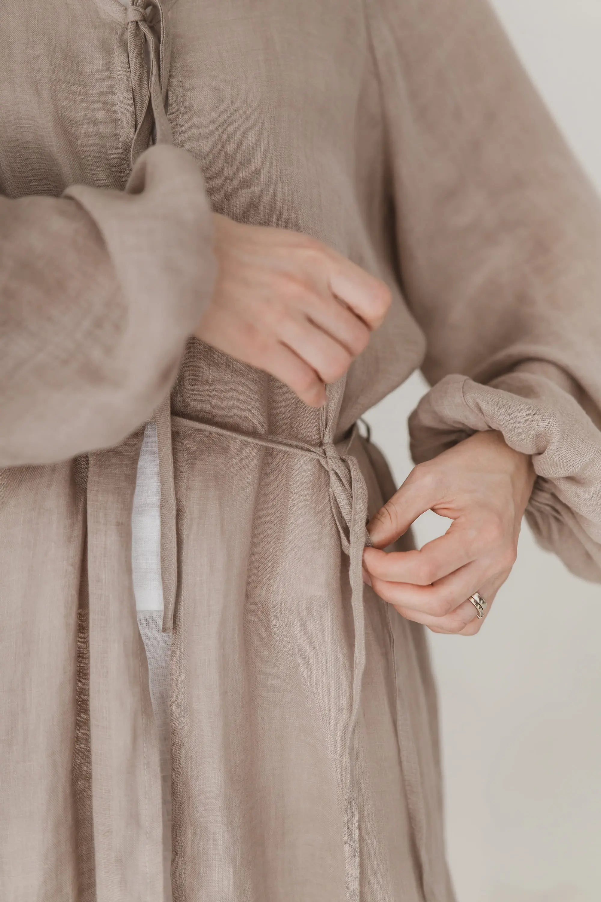 Close-up of hands tying the waist tie on a natural linen kaftan