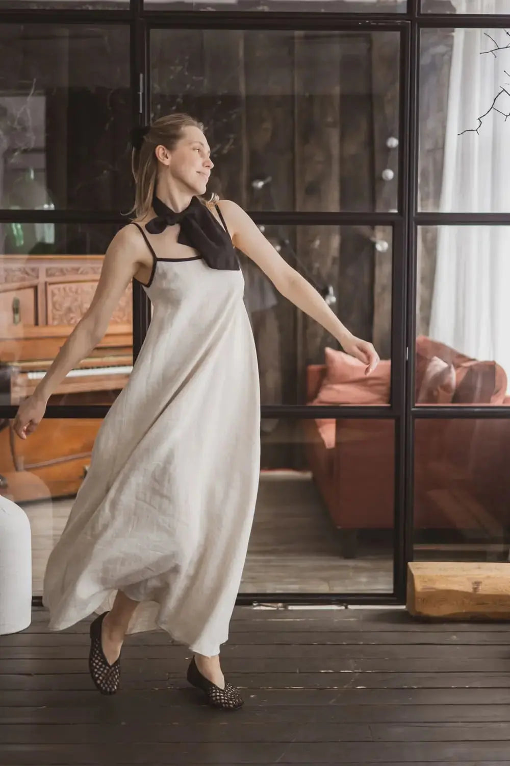 Woman in a flowing natural linen maxi slip dress with contrast black trim, full length front view in motion