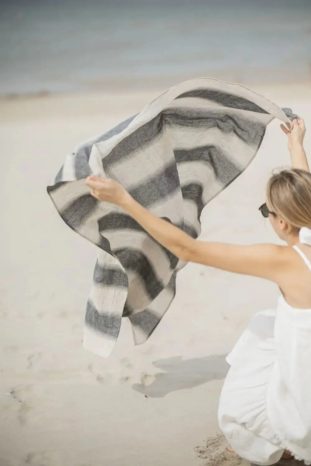 Linen Huckaback Beach Towel in natural gray striped, blowing in the wind on the beach