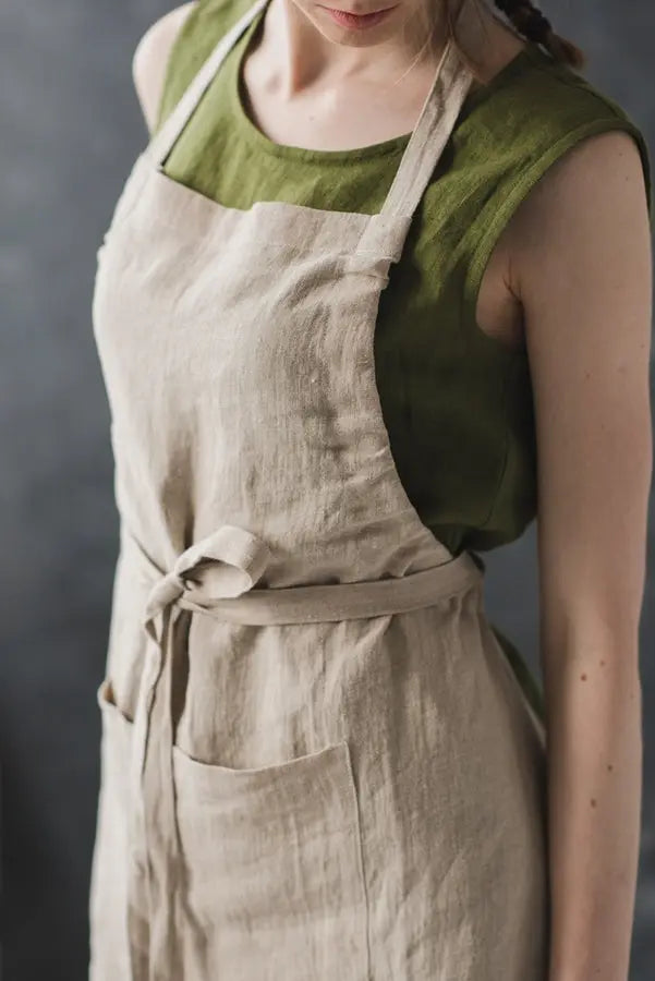 A close up of a woman wearing a Bib style long linen apron with a front pocket and adjustable straps.