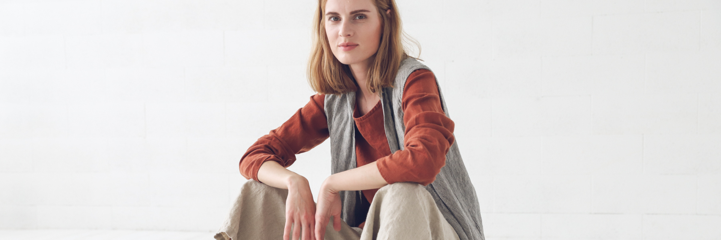 A woman sitting, wearing linen clothing.
