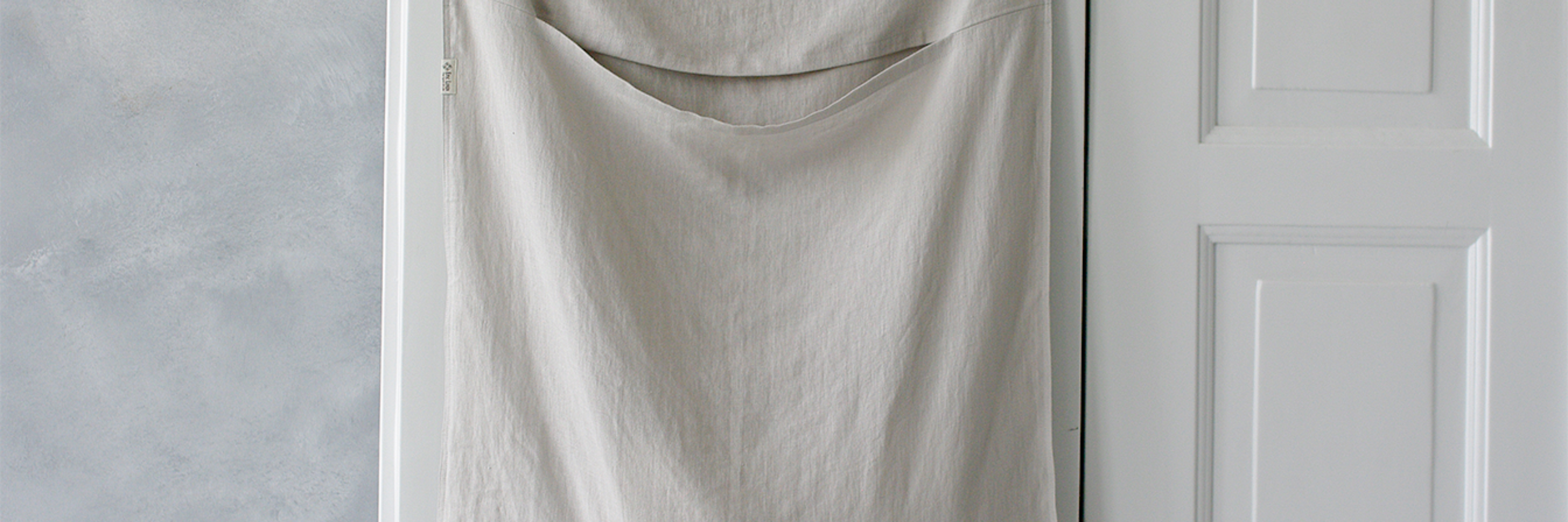 A white hanging linen laundry bag on a door.