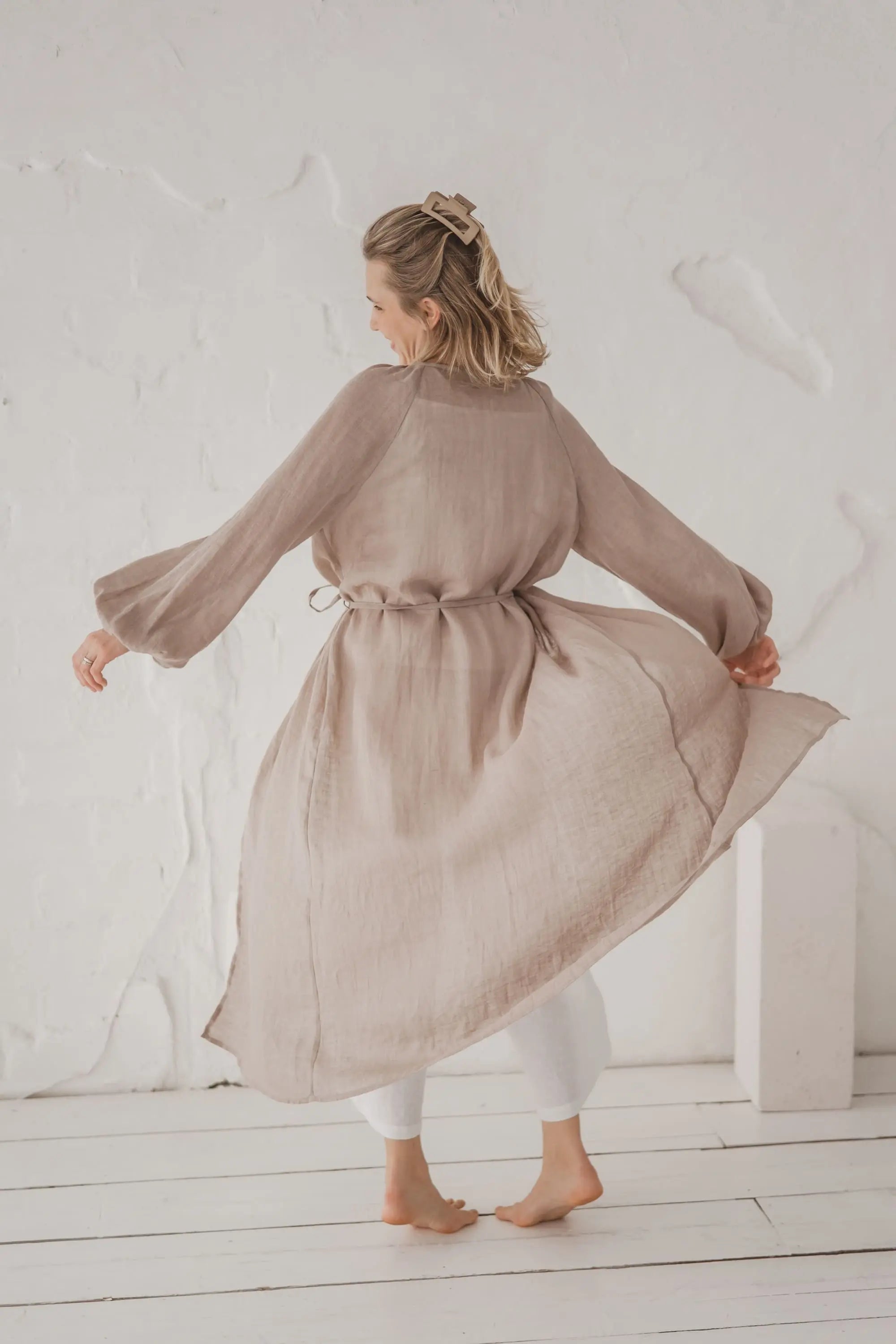 Full back view of a natural linen kaftan in motion, flowing silhouette with waist tie