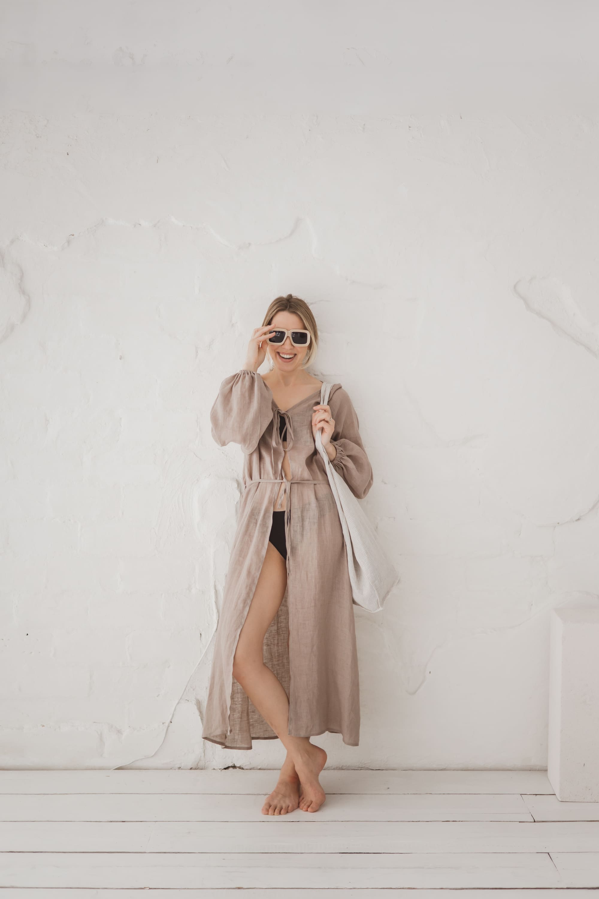 Woman wearing a flowing natural linen kaftan with long sleeves and waist tie, full length front view