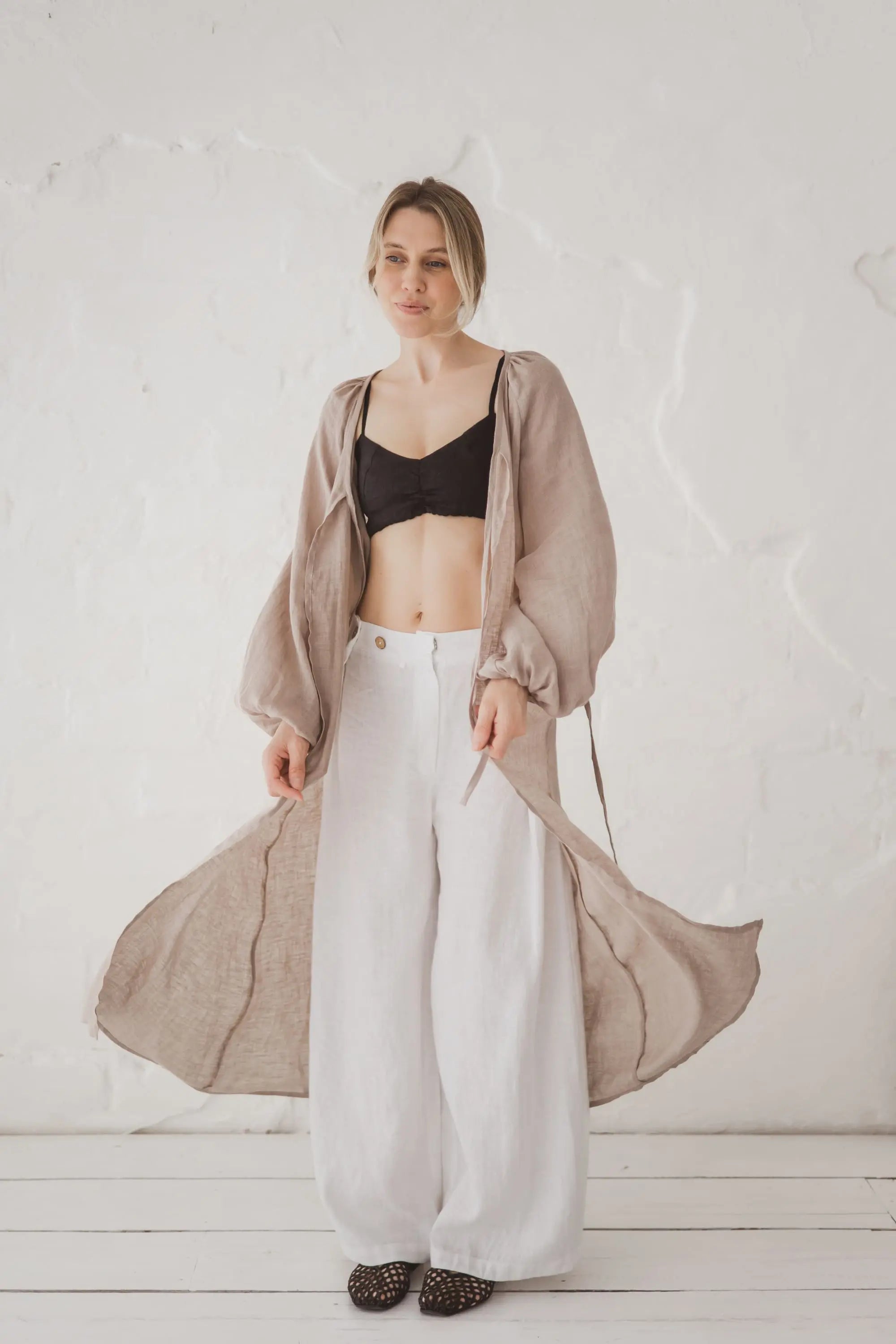 Woman in a natural linen kaftan open and flowing, styled with wide-leg white linen trousers, full length front view