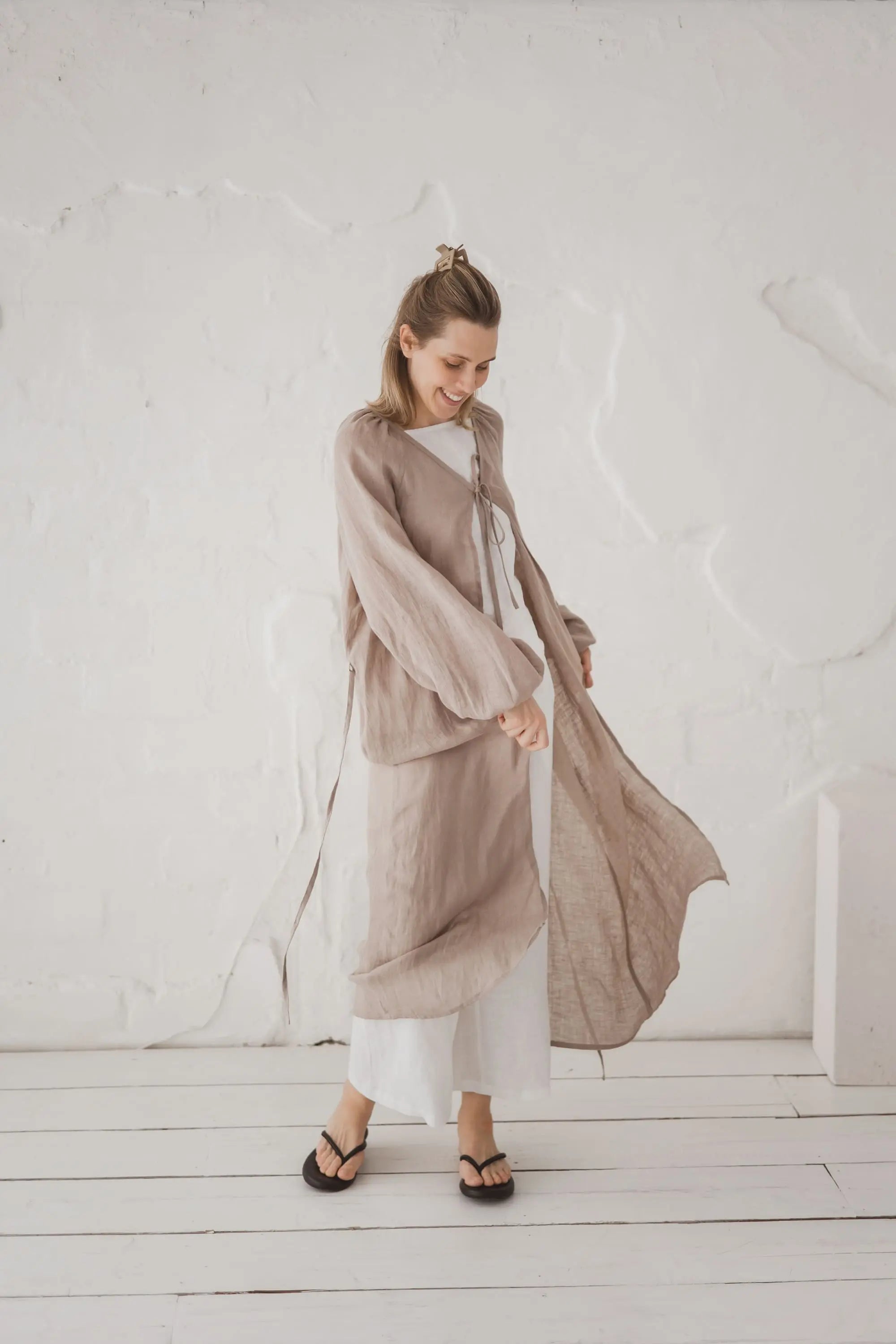 Woman in an open natural linen kaftan with long sleeves, full length front view, styled over white trousers