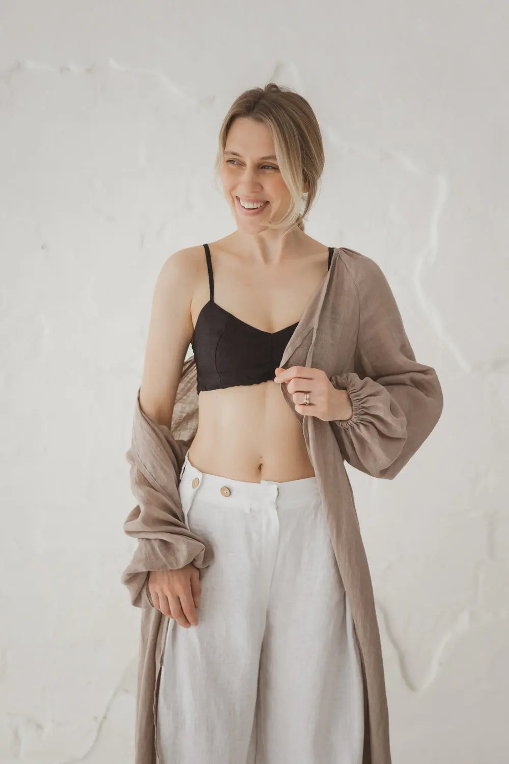 Woman wearing an open natural linen kaftan styled with wide-leg white linen trousers, upper body view