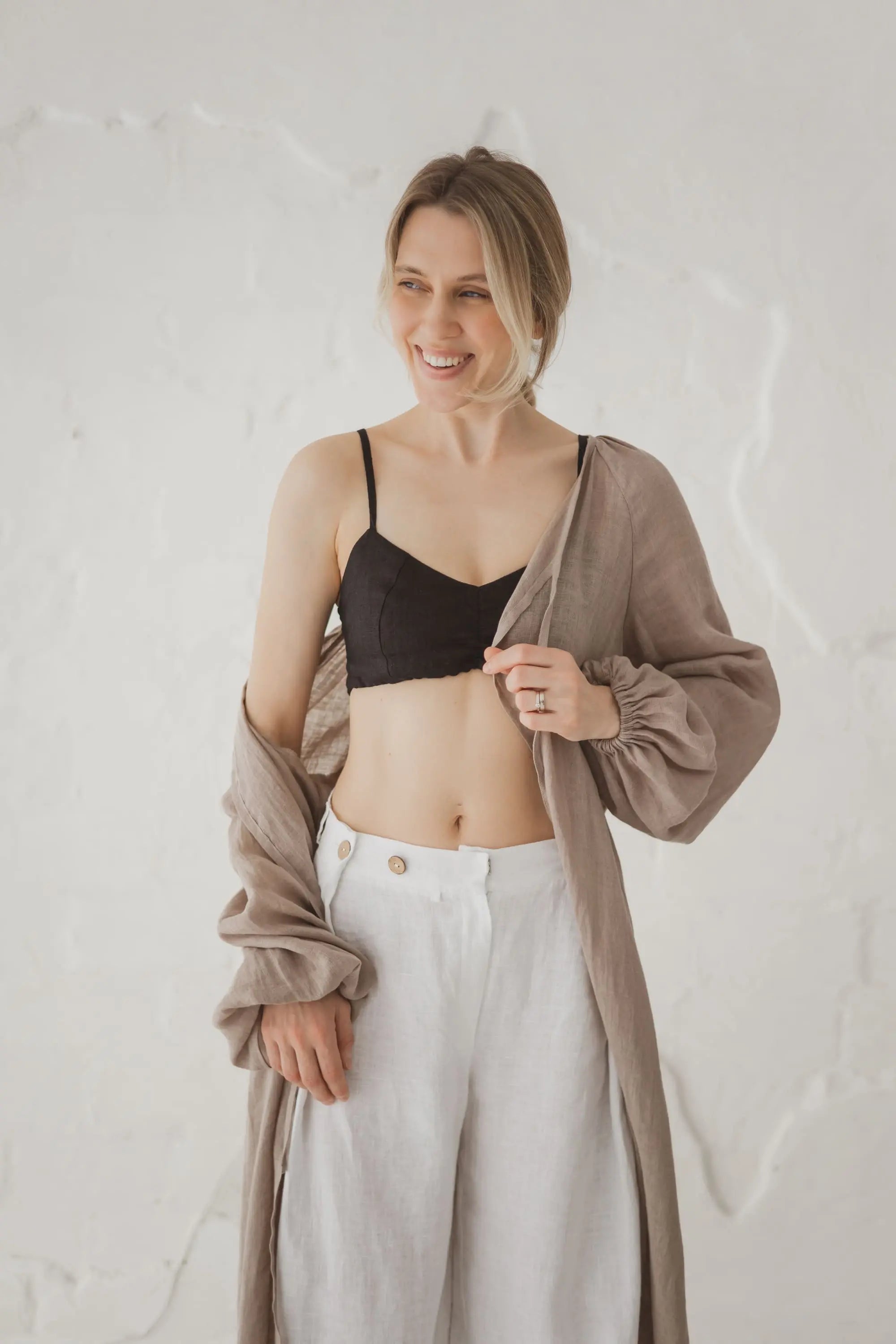 Woman wearing an open natural linen kaftan styled with wide-leg white linen trousers, upper body view