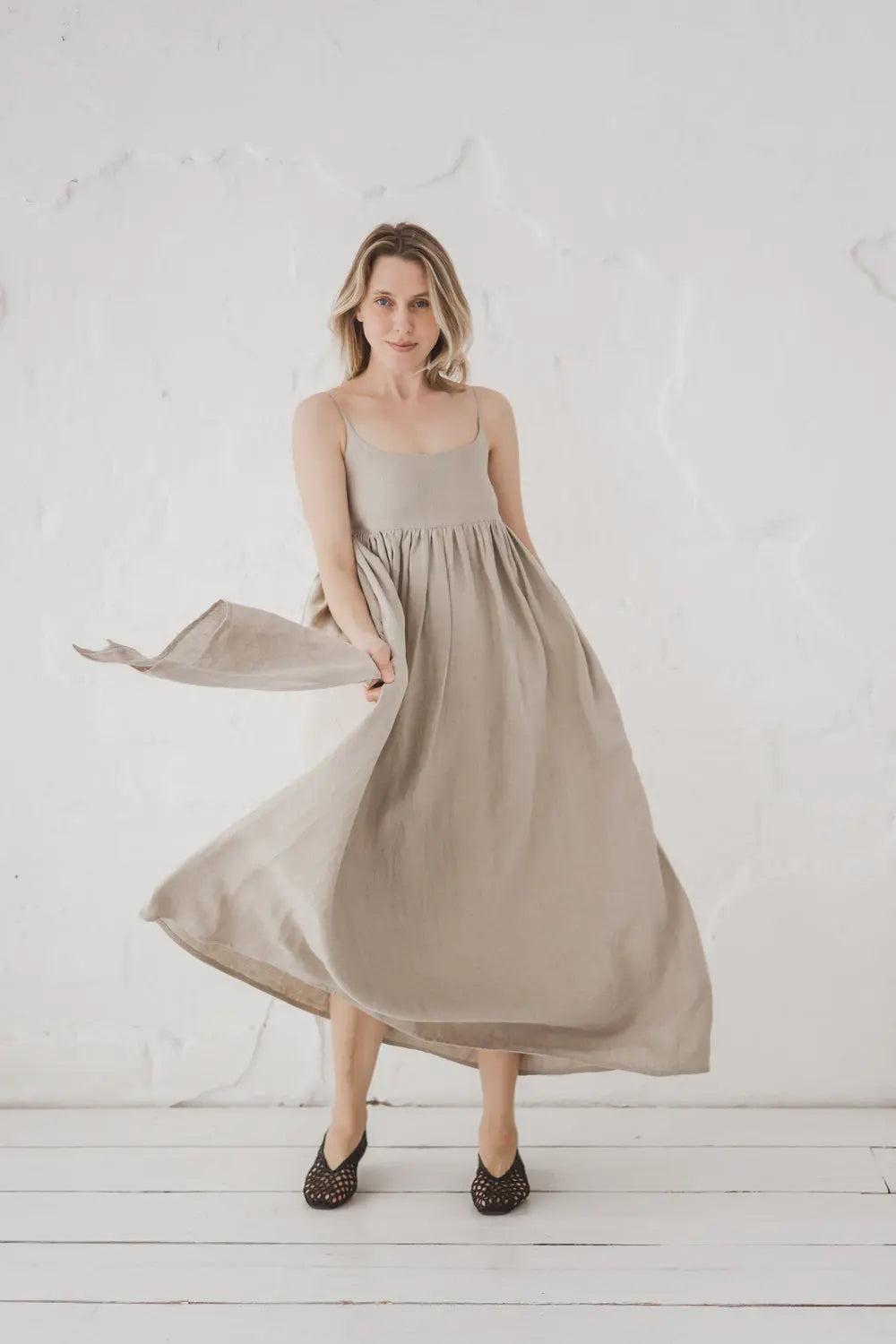 Woman in a flowing natural linen maxi dress with spaghetti straps, full body front view in motion