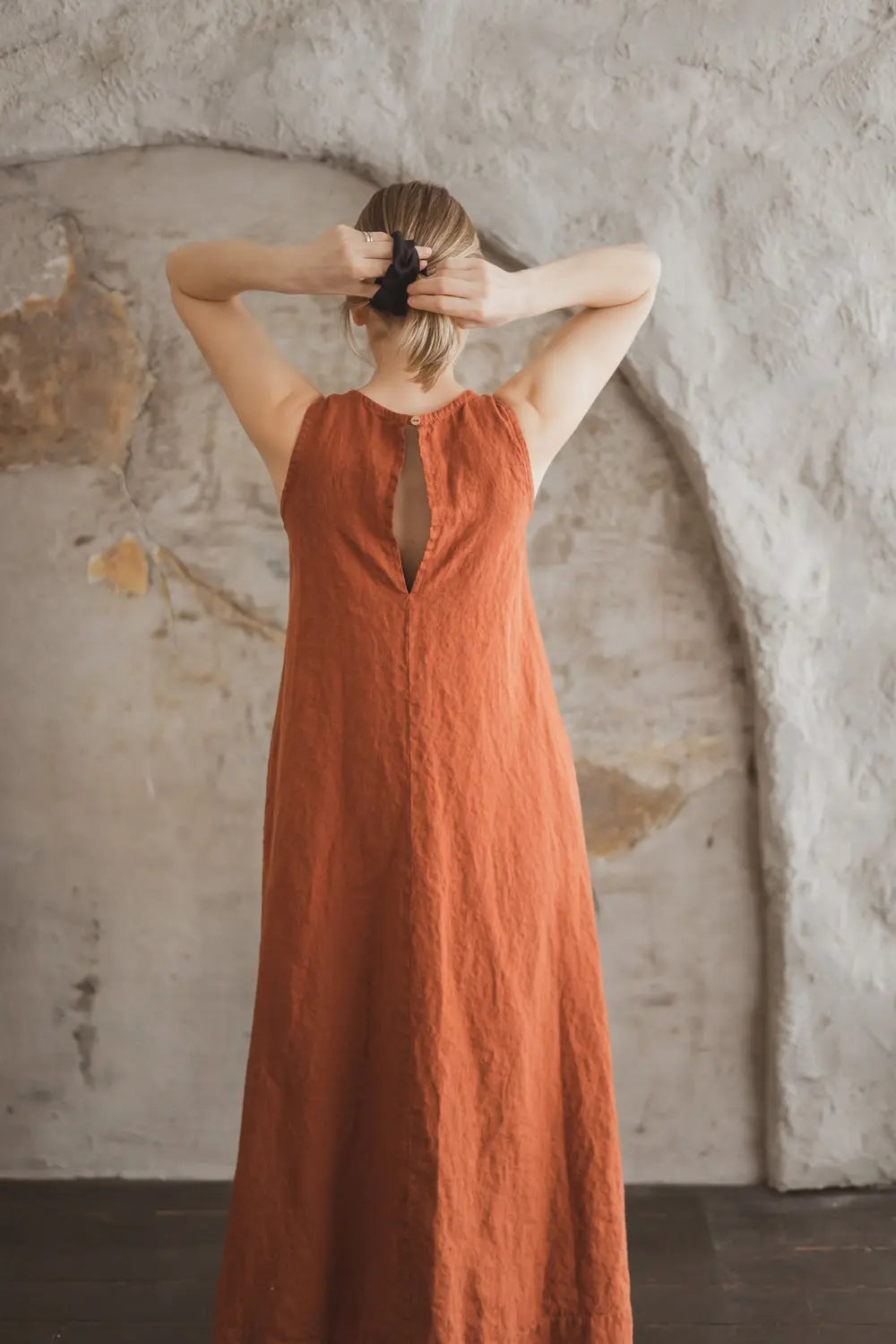 Back view of a sleeveless linen maxi dress showing open back with button detail