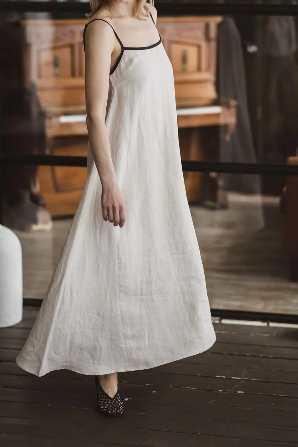 Side view of a natural linen maxi slip dress with contrast black trim and spaghetti straps, full length