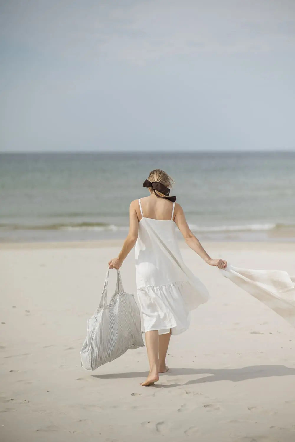 Woman carrying Linen Huckaback Beach Towel in white natural striped, walking on the beach
